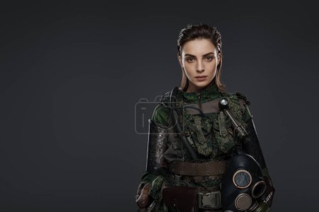 Photo for Portrait of a woman in military attire, portraying a rebel or partisan, against a gray background, depicting a Middle Eastern conflict - Royalty Free Image