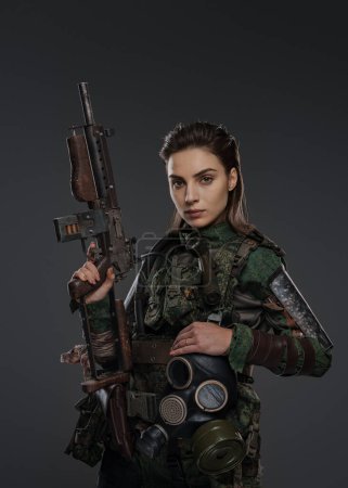 Foto de Retrato de una soldado con atuendo militar, sosteniendo un rifle automático hecho en casa, que representa a un rebelde o partisano en un conflicto de Oriente Medio sobre un fondo gris - Imagen libre de derechos