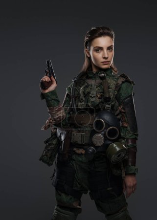 Foto de Guerrera vestida de rebelde o partidista con atuendo militar, armada con una pistola, colocada sobre un fondo neutral, representando agitación en el Medio Oriente - Imagen libre de derechos