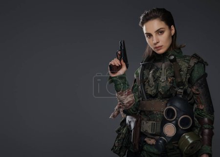 Téléchargez les photos : Guerrière habillée en rebelle ou partisane en tenue militaire, armée d'un pistolet, placée sur un fond neutre, représentant la tourmente au Moyen-Orient - en image libre de droit