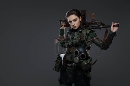 Téléchargez les photos : Portrait d'une femme soldat en tenue militaire, tenant un fusil automatique fait maison, représentant un rebelle ou un partisan dans un conflit au Moyen-Orient sur fond gris - en image libre de droit