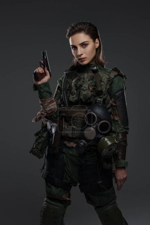 Foto de Retrato de una soldado en uniforme militar con una pistola, encarnando a un rebelde o partisano en un conflicto de Oriente Medio contra un fondo gris - Imagen libre de derechos