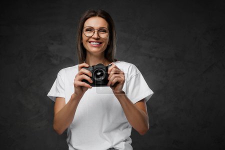 Téléchargez les photos : Joyeuse photographe en lunettes et tee-shirt blanc avec son appareil photo, dans un contexte lunatique - en image libre de droit