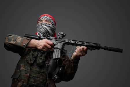 Foto de Soldado fanático radical de Oriente Medio vestido con un keffiyeh blanco y un uniforme de campo camuflado, armado con un rifle automático, sobre un fondo gris - Imagen libre de derechos