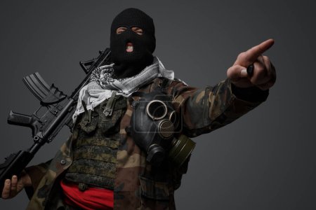 Téléchargez les photos : Soldat fanatique radical du Moyen-Orient, vêtu d'une cagoule noire et d'un uniforme de campagne camouflé, armé d'un fusil, pointant menaçant dans une certaine direction - en image libre de droit