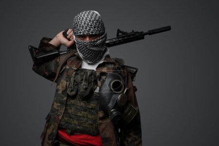 Foto de Soldado fanático radical de Oriente Medio vestido con un keffiyeh blanco y un uniforme de campo camuflado, armado con un rifle automático, sobre un fondo gris - Imagen libre de derechos