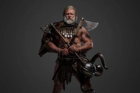 Guerrier viking âgé grizzli, affichant force et sagesse, vêtu de fourrures et d'armure légère, avec un casque suspendu à la taille, brandissant deux haches sur un fond neutre