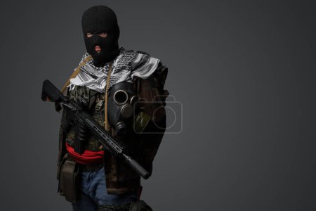 Foto de Retrato de un militante de Oriente Medio, con un traje de pasamontañas y camuflaje negro, sosteniendo un rifle, montado sobre un fondo gris - Imagen libre de derechos