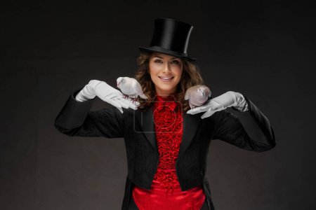Téléchargez les photos : Magicienne en tenue de magicienne et chapeau noir, mettant en valeur ses talents magiques avec des colombes blanches gracieuses dans un mystérieux fond sombre - en image libre de droit