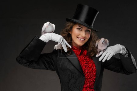 Téléchargez les photos : Image captivante d'une magicienne vêtue de magicien et coiffée d'un haut-de-forme noir, mettant en valeur ses talents de magicienne avec des colombes blanches gracieuses dans un mystérieux fond sombre - en image libre de droit