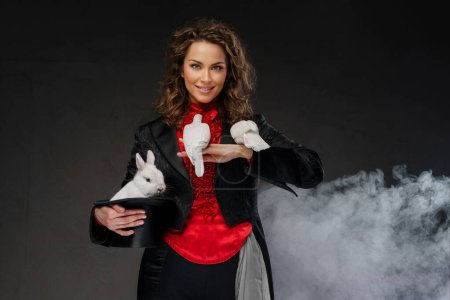Photo for A portrait of a magician in a magicians costume and black top hat performing magic tricks with white doves against a dark background - Royalty Free Image