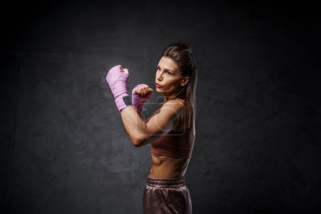 Photo for Muscular woman boxer demonstrating striking skills, dressed in sports attire, against a moody dark backdrop - Royalty Free Image