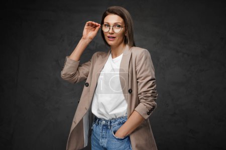 Foto de Mujer con estilo en gafas, camiseta y chaqueta golpea una pose contra un fondo oscuro - Imagen libre de derechos