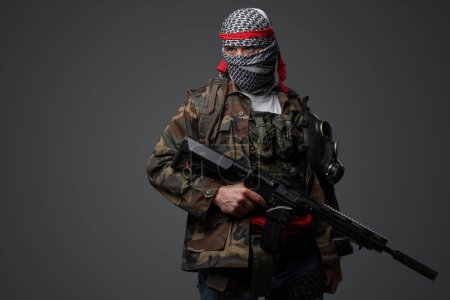 Photo for Militant from the Middle East, dressed in a white keffiyeh and camouflaged field attire, wielding an automatic rifle, set against a neutral gray backdrop - Royalty Free Image