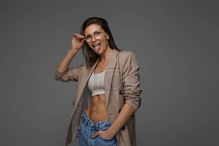Photo for Smiling, chic lady in athletic bra and jacket radiates happiness on a gray backdrop - Royalty Free Image