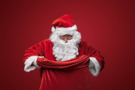 Photo for Santa Claus in his classic red suit, confidently holding a bag - Royalty Free Image