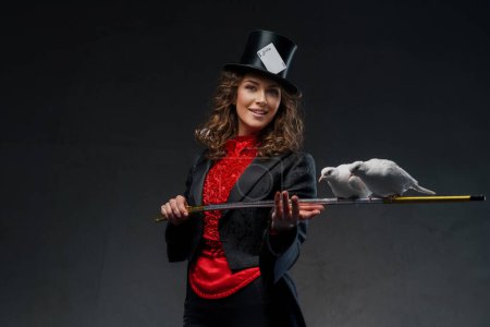 Foto de Un retrato de un mago disfrazado de magos y sombrero de copa negro realizando trucos de magia con palomas blancas contra una oscuridad - Imagen libre de derechos