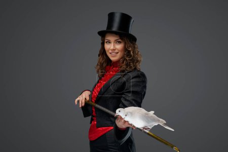 Téléchargez les photos : Portrait d'un magicien en costume de magicien et chapeau noir exécutant des tours de magie avec des colombes blanches sur un fond sombre - en image libre de droit