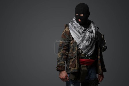 Foto de Un soldado radical de Oriente Medio vestido con pasamontañas negro y camuflado uniforme de campo, armado con un rifle, sobre un fondo gris - Imagen libre de derechos