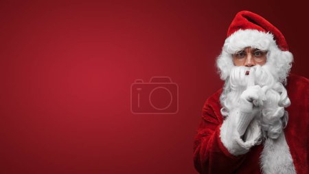 Photo for Santa Claus gesturing silence with finger on lips, mysterious holiday secret concept - Royalty Free Image