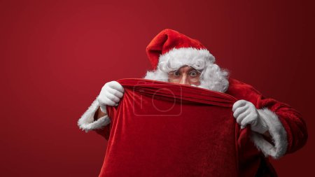 Foto de Santa Claus mirando por encima de un saco rojo, ojos llenos de emoción navideña - Imagen libre de derechos