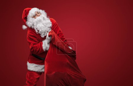Téléchargez les photos : Père Noël portant un sac lourd, prêt à livrer des cadeaux de Noël - en image libre de droit