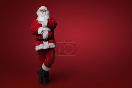 Téléchargez les photos : Père Noël réfléchissant, avec une pose réfléchie sur fond rouge - en image libre de droit