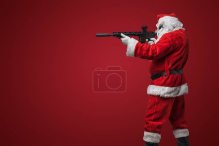 Photo for A man dressed as Santa Claus, wearing sleek black sunglasses, poses with toy machine guns against a bold red backdrop - Royalty Free Image