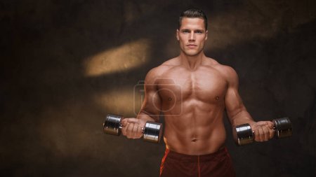 Toned athlete in workout session with heavy dumbbells against dark background