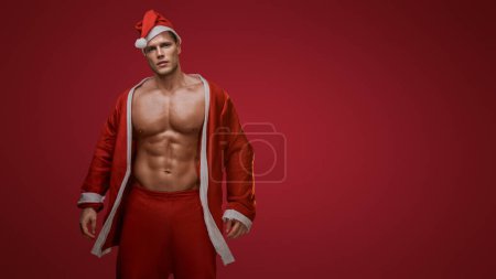 Foto de Santa en modo fitness, mostrando los músculos sobre un fondo rojo - Imagen libre de derechos