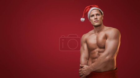 Téléchargez les photos : Père Noël en mode fitness, montrant les muscles sur fond rouge - en image libre de droit