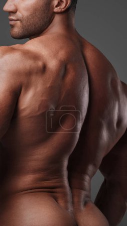 Foto de Vista desde atrás de un hombre musculoso con un torso desnudo, golpeando una pose, mostrando sus músculos tensos sobre un fondo gris - Imagen libre de derechos