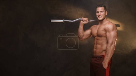 Photo for Smiling muscular man with a curl bar in a moody gym atmosphere - Royalty Free Image