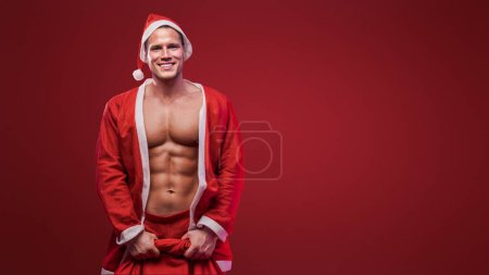 Photo for Cheerful Santa holding a gift sack, combining holiday joy with a fit physique - Royalty Free Image
