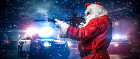 Téléchargez les photos : Un homme déguisé en Père Noël, visant avec une mitrailleuse, pose devant des voitures de police avec de nombreuses lumières et sirènes de police, au milieu d'une nuit de tempête enneigée dans la rue - en image libre de droit