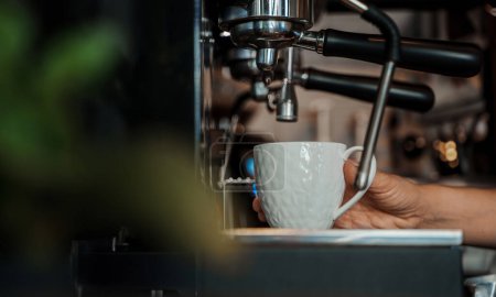 Foto de Una intrincada cafetera espresso vierte café fresco en una elegante taza blanca, capturando la esencia de una vibrante cafetería - Imagen libre de derechos