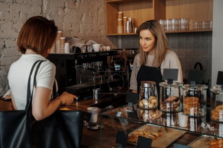 Photo for A beautiful and smiling barista serves a customer in a coffee shop - Royalty Free Image