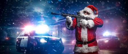 Foto de Un hombre vestido de Santa Claus, apuntando con una ametralladora, posa frente a coches de policía con numerosas luces y sirenas policiales, en medio de una noche nevada y tormentosa en la calle - Imagen libre de derechos