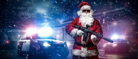 Foto de Un hombre vestido de Santa Claus, sosteniendo una ametralladora, posa frente a coches de policía con numerosas luces y sirenas policiales, en medio de una noche nevada y tormentosa en la calle - Imagen libre de derechos