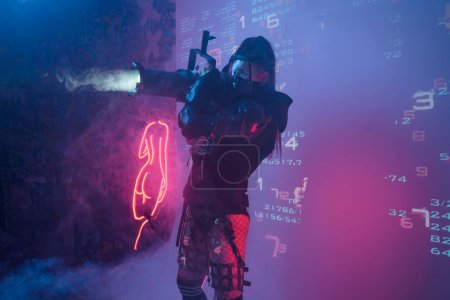 Foto de Una mujer con un traje negro táctico futurista sostiene un gran proyector que se asemeja a un cañón de luz, de pie sobre un telón de fondo de símbolos digitales proyectados - Imagen libre de derechos