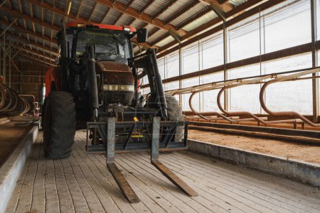 Foto de La parte posterior de un gran tractor negro que muestra la cabina y los neumáticos, alojados en un granero agrícola de madera - Imagen libre de derechos