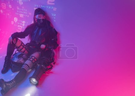 Téléchargez les photos : Une figure féminine, vêtue d'un ensemble noir tactique futuriste, s'incline sur le sol avec un projecteur de taille importante sur fond de symboles numériques projetés - en image libre de droit