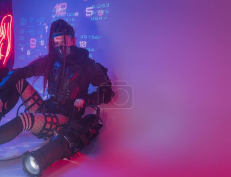 Photo for A female figure, dressed in a futuristic tactical black ensemble, reclines on the ground with a sizable projector against a backdrop of projected digital symbols - Royalty Free Image