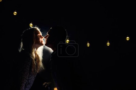 Photo for Romantic couple kissing over candlelit dinner in a night restaurant. Red wine glasses and decorative elements on the table. Dark interior with warm lighting - Royalty Free Image