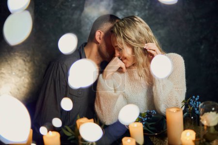 Foto de Una pareja romántica en un restaurante débilmente iluminado con velas parpadeantes, el hombre susurrando dulces cosas en el oído de su amante. - Imagen libre de derechos