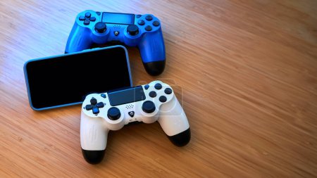 Weiße, blaue Gamepads und Smartphones auf dem Tisch. Gamer und Spielkonzept, Spiel auf dem Smartphone. Gaming Set Hintergrund mit Kopierraum