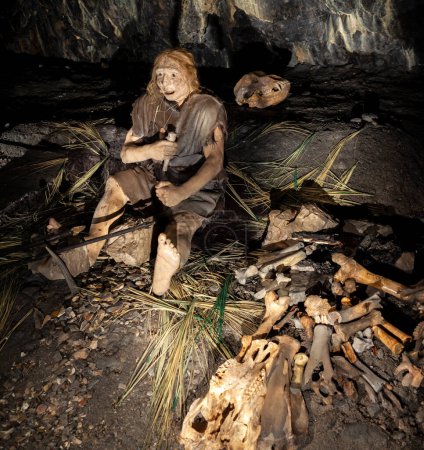 Photo for Reconstruction of a Middle Palaeolithic scene in the Grotta Nera. Primal tribe of ancient wild people animal skin and stone axes eating frying meat on bonfire staying in cave. Neanderthals. Ice age. Basovizza Trieste - Royalty Free Image