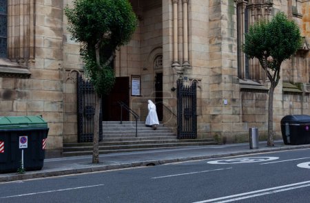 Foto de Bilbao, España - 03 de agosto de 2022: Una monja vestida con un hábito blanco está subiendo las escaleras de la iglesia de San Francisco de Asís también conocida como La Quinta Parroquia - Imagen libre de derechos