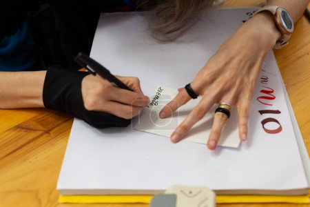 Großaufnahme der Hände einer erfahrenen Kalligraphin, die auf einem Skizzenbuch das Schreiben in italienischer Sprache und im antiken Stil übt, Datum 26. Oktober