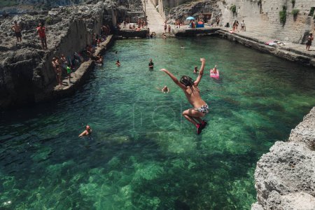 Téléchargez les photos : Marina Serra, Italie - Juillet 2023 : les enfants sautent dans l'eau cristalline d'une piscine naturelle de la mer - en image libre de droit